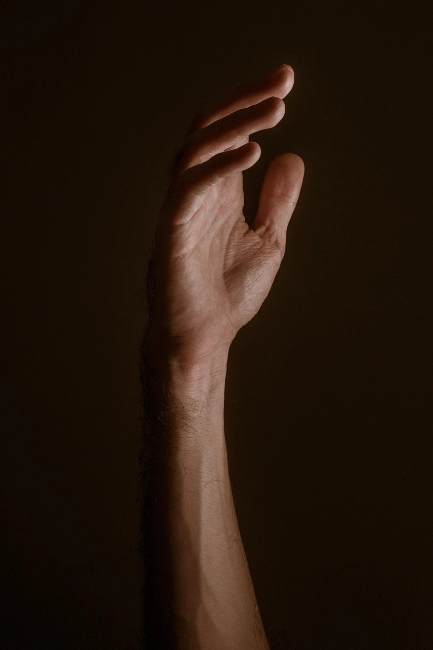 Raising hands in prayer — the biblical posture of asking Person standing with hands raised toward a sunlit sky, representing the act of asking God in prayer