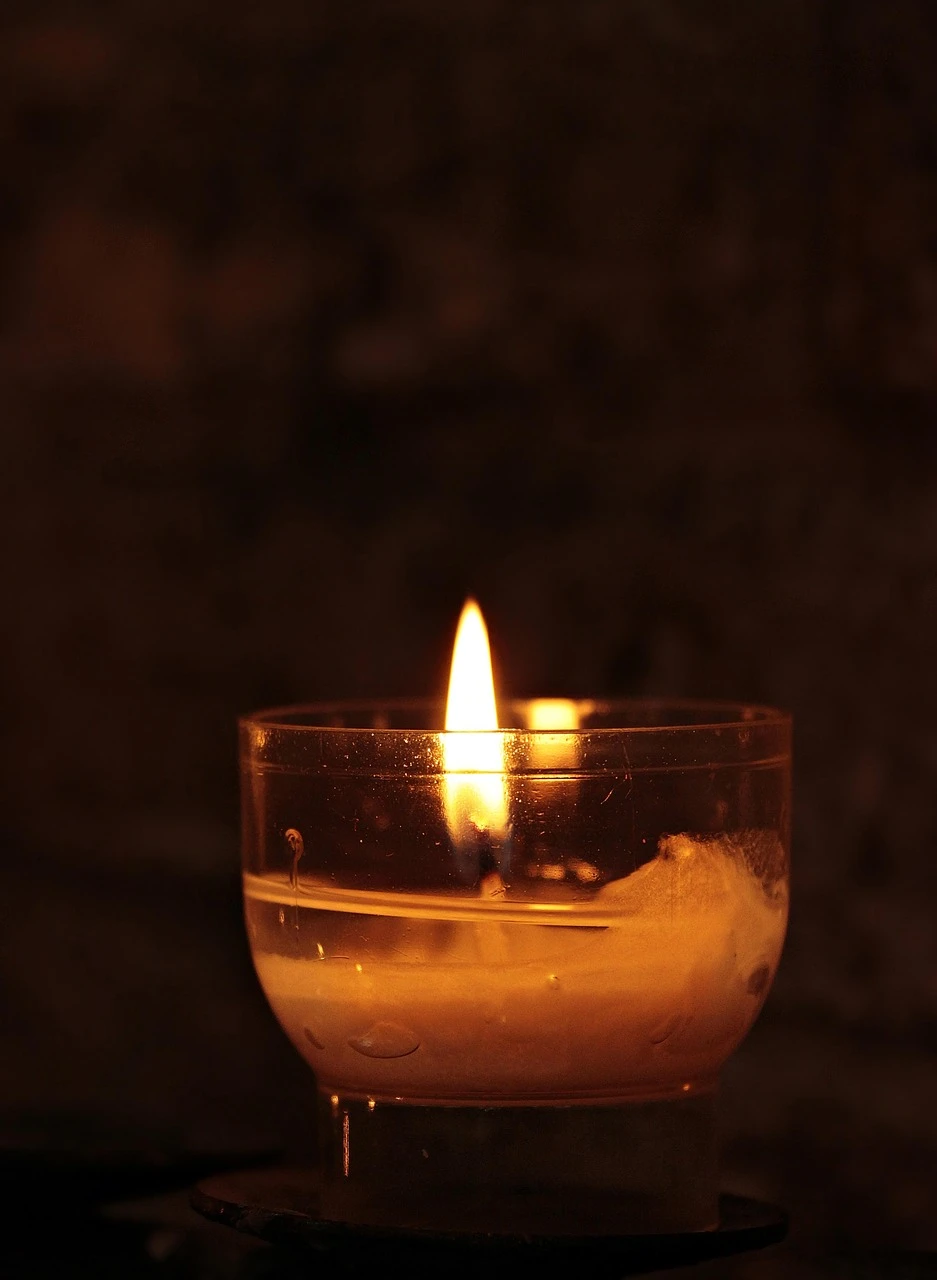 A person's hands in quiet prayer at a table, a simple candle burning beside them